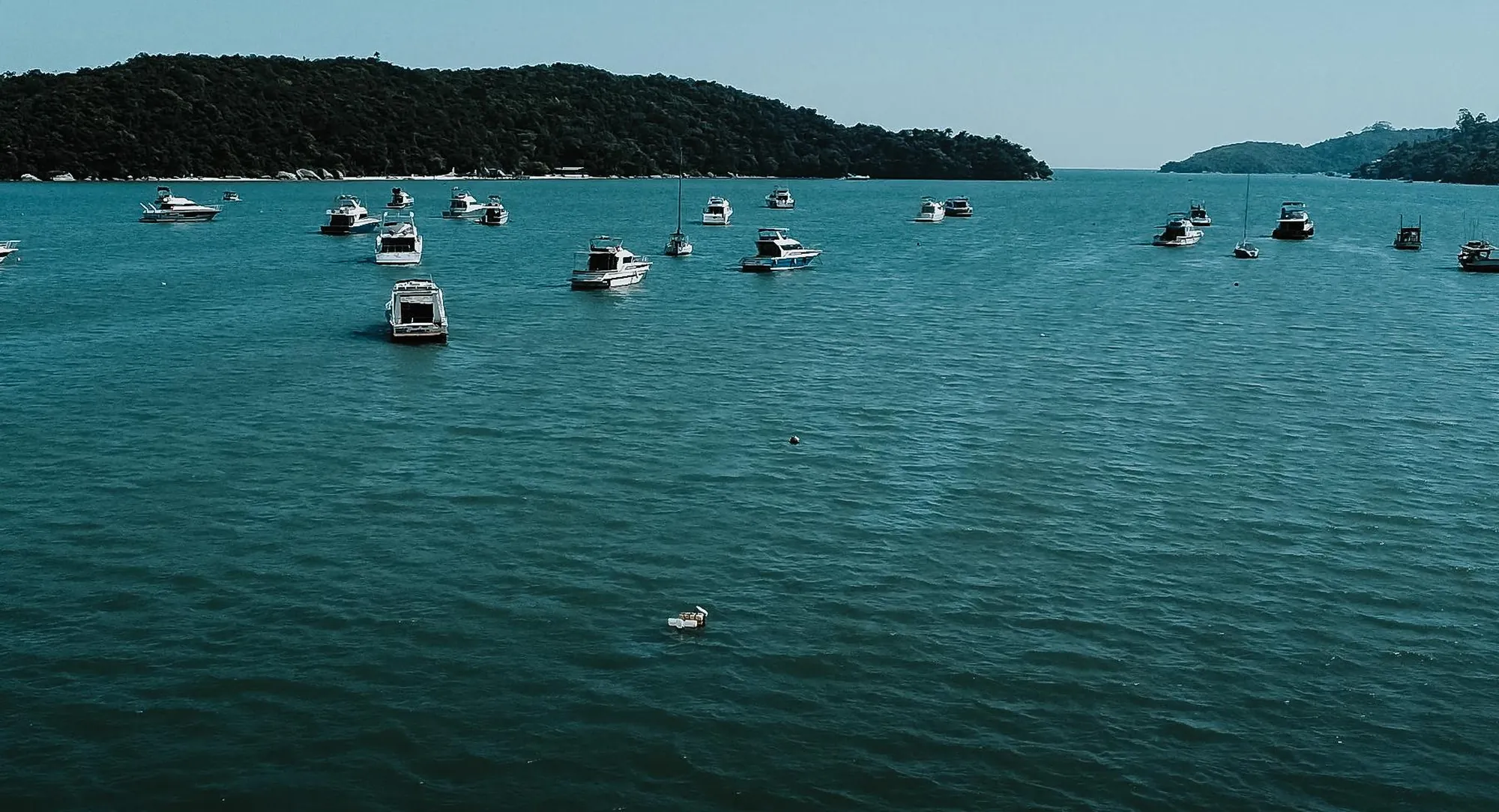 Baía de Porto Belo, na Costa Esmeralda, com barcos ancorados em águas esverdeadas e a mata atlântica ao fundo